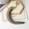 Coda di peluche grigia su fondo bianco, con chiusura dorata e manicotto decorato con strass - Grigio