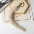Primo piano di un ciondolo a coda color crema, soffice, con chiusura a strass e anelli dorati - Bianco perla