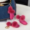 Trois breloques roses, gant et bottes à pompons doux, avec clips dorés près d’un sac en jean - Rose rouge