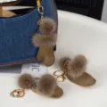 Trois breloques brunes en suédine avec pompons doux et attaches dorées près d’un sac en jean - Vert matcha