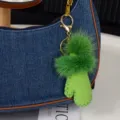 Gros plan de pompons verts et d'un charm effet daim avec mousqueton doré sur un sac en jean - Vert clair