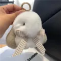 Nahaufnahme eines flauschigen Hasenanhängers in Weiß und Beige mit Karoschleife und Metallring - Gebrochenes Weiß