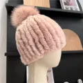 Side view of a pink rib-knit winter hat, highlighting its plush texture and fluffy pom-pom - One Size (Elastic) / Dusty Pink