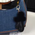 Gros plan : pompon noir et charm en cuir fixés à un sac en denim bleu avec mousqueton doré - Noir Verni