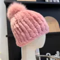 Close-up of a pink ribbed knit hat with plush texture and a fluffy pom-pom on a display head - One Size (Elastic) / Dusty Pink