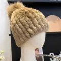 Side view of the camel-toned hat, showing its plush knitted texture and fluffy pom-pom - One Size (Elastic) / Camel