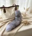 Gray fluffy real fox fur tail bag charm with gold-tone hook and chain clasp, shown on a handbag - Silver Blue Fox Tail