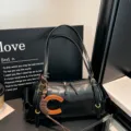 Black cylindrical shoulder bag with twin straps, metal fittings and a wooden C-shaped charm - Black