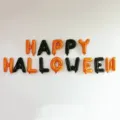 HAPPY HALLOWEEN foil letter balloons in orange and black, displayed in two rows on a wall - HAPPY HALLOWEEN Letters / 16 Inch Letter Balloon Set