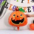 Shiny orange foil pumpkin balloon with a smiling face, green leaves and brown stem on display - Green Leaf Pumpkin Foil Balloon / 2 Pieces Set (63cm*48.5cm)