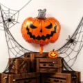 Halloween display with an orange foil pumpkin face balloon, gray stem, webs and wooden crates - Ghost Face Pumpkin Foil Balloon / 2pcs Pack (73cm*61.5cm)