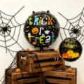 Two black foil balloons with colorful Halloween prints displayed among spiderwebs and wooden crates - 18 Inch Round Black Halloween Foil Balloon / 2 Pieces Pack