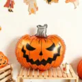 Ballon citrouille en aluminium orange, visage grimaçant noir, présenté sur une étagère en bois - Citrouille d'Halloween