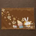 Flat view of a brown placemat with floral lace motifs and a playful cartoon pig and rabbit - Forest Animal Friends (MZBA072403) / 40x30cm