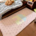 Pink plush bedside runner rug with pastel cartoon house and star patterns, shown beside a bed - 60x40cm / Pink (House Bear)