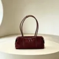 Burgundy suede-textured bag with leather trim, twin handles and a silver zipper on a display plinth - Burgundy