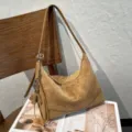 Tan suede shoulder bag with curved silhouette, zipper, and tassel, styled on an open magazine - Size: 30-10-20cm / Camel