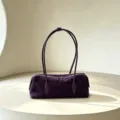 Purple suede-textured bag with long handles and top zipper, displayed on a pale round table - Purple
