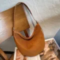 Close-up of brown suede texture, braided strap, and silver clasp on a crescent shoulder bag - 30x6x25.5cm / Brown