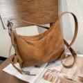 Brown suede-textured bag on a tabletop, with a zip opening, leather strap and silver hardware. - Size: 30-10-20cm / Brown
