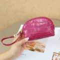 Close-up of a fuchsia crocodile-embossed pouch with gold zipper and wrist strap, held in hand - 15x5x10cm / Misty Rose Red