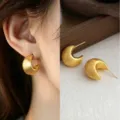Close-up of a matte brushed gold crescent earring worn on the ear, with its matching pair displayed flat - Pointed C-Shaped Earrings (3925)