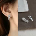 Close-up of a silver three-rose earring worn on the ear, with its matching pair displayed beside it - Triple Rose Flower (4493) / Silver