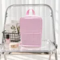 Pink-and-white seersucker stripes and top handle on a zippered pouch, displayed on a clear chair - Pink