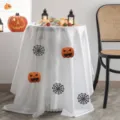 White Halloween tablecloth with orange pumpkin faces and black spiderwebs draped over a round table - Ghost Shaped Style (TVA02) / 60x40cm (Small Cover Cloth)