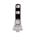 Close-up of an ornate silver-tone medallion with a pink stone and dangling bell charms on velvet - Pink