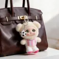 Cream plush bear bag charm in a pink striped top, with a soccer ball pendant and metal clip - Beige