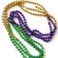 Overhead view of glossy gold, purple, and green round beads layered in loose strands on white - 3 Pieces/Pack