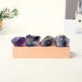 Cuatro cristales naturales en bruto de color violeta sobre una base de madera clara con luz tenue - Fluorita Arcoíris