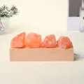 Lámpara nocturna de sal rosa anaranjada, con cuatro piedras naturales sobre una base de madera clara - Sal Naranja