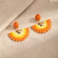 Close-up of orange and yellow woven fan-shaped earrings with gold-tone bead accents on linen - Orange (E2882)