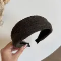 Close-up van een brede, donkerbruine gebreide haarband in de hand, met zwarte stoffen voering - Koffie
