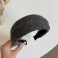 Close-up van een brede donkergrijze haarband met wolachtige textuur, zwarte voering en nette randen. - Grijs