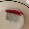 Close-up of a curved red resin comb with slim metal teeth and FRANCE Handmade lettering - Red Gold Label Oval Comb