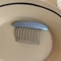 Blue-gray resin comb with silver metal teeth rests on a beige ceramic plate, with small lettering. - Blue Gold Label Oval Comb