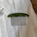 Flat lay showing a curved green marbled comb, silver teeth, and embossed lettering on linen - Green Multicolor Comb