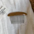 Close-up of a brown resin hair comb with a curved back, silver metal teeth and engraved lettering - Brown Multicolor Comb