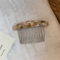 Close-up of a curved comb with mottled brown resin back and slender silver metal teeth - Marble Gold Label Comb