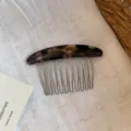 Curved tortoiseshell-look resin comb with slim metal teeth displayed on natural linen fabric - Black Coffee Gold Label Comb