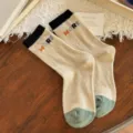 Beige knitted mid-calf socks with black ribbed cuffs, green toes, and colorful MORE lettering - One Size / Beige