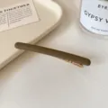 Barrette fine en métal vert olive mat avec pince dorée, présentée à plat sur un fond clair - Brun Clair