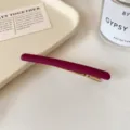 Barrette longue bordeaux mat avec pince en métal doré, présentée sur un tissu clair - Rose rouge