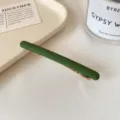 Barrette droite vert mat avec une fine pince métallique dorée, présentée en diagonale sur un tissu clair. - Vert