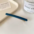 Barrette à cheveux bleu mat avec pince dorée, présentée en diagonale sur un fond en tissu clair - Bleu