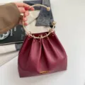Primer plano de un bolso burdeos fruncido, con asa de aro dorada y tachuelas metálicas decorativas - Rojo
