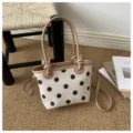 Borsa a pois con manici beige annodati e tracolla rimovibile, su un tappeto accanto ai libri - senza ciondolo / Bianco